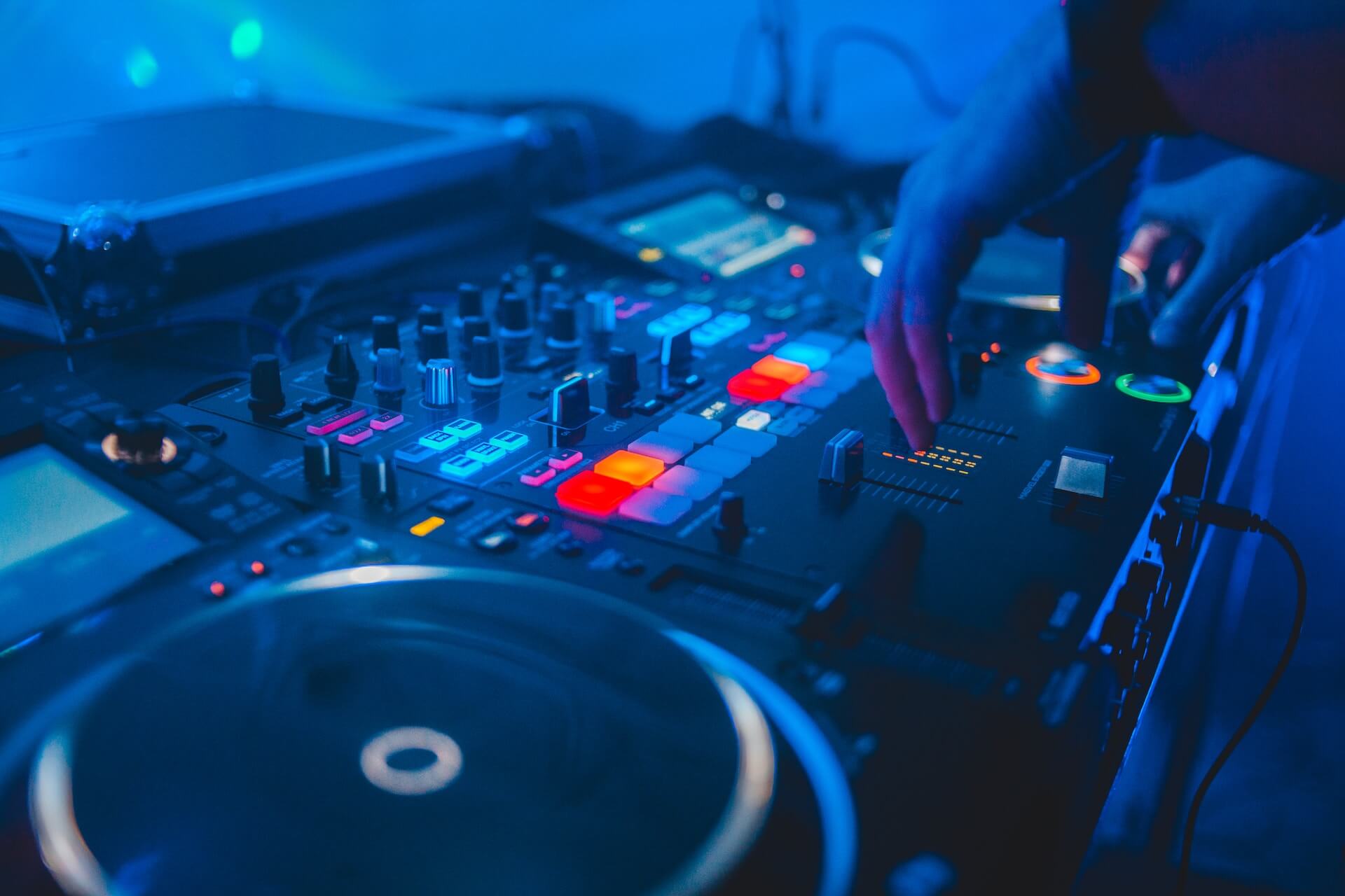 A DJ table with a mixer, turntables, and headphones, with colorful lights pulsating in the background, creating a vibrant atmosphere while trance music fills the air.